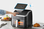 Midea air fryer MF-CY85WK2 8.5L on a kitchen counter with a hand pressing the button, surrounded by fruits and a croissant.