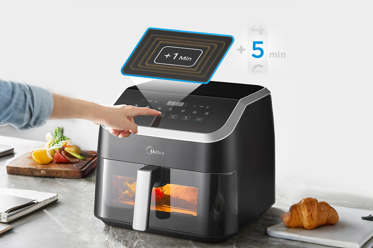 Midea air fryer MF-CY85WK2 8.5L on a kitchen counter with a hand pressing the button, surrounded by fruits and a croissant.