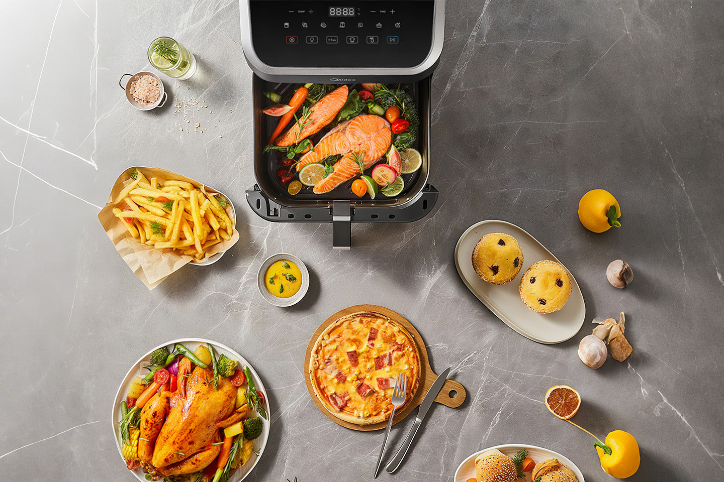 Midea MF-CY85WK2 8.5L air fryer with various food items on a kitchen surface